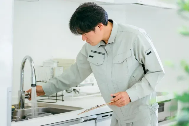 作業着姿の人が台所の蛇口からお湯を出して確認しているイメージ写真