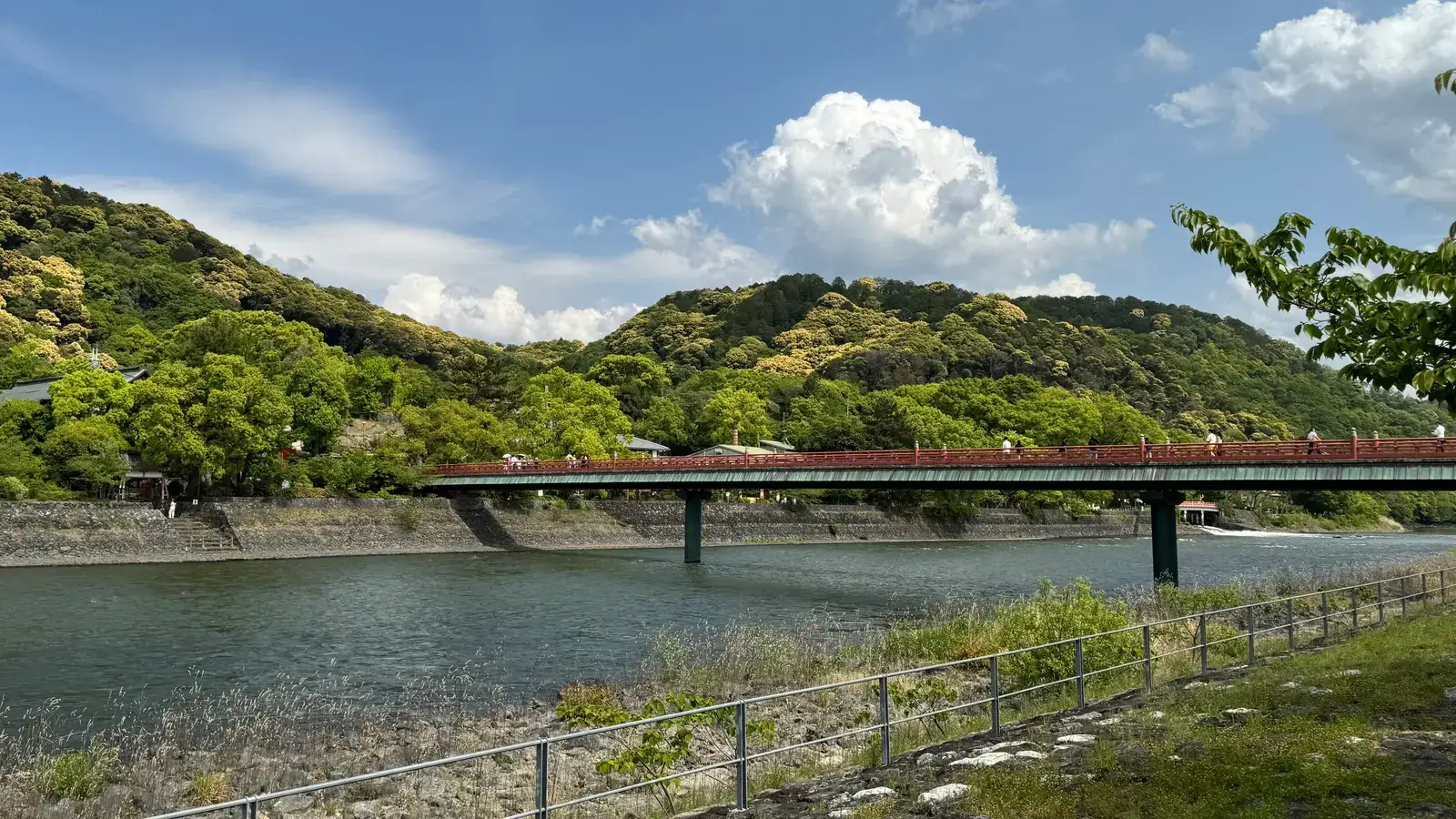 宇治川に架かる赤い欄干の朝霧橋。奥に緑の山並みと、青空に白い雲が広がっている